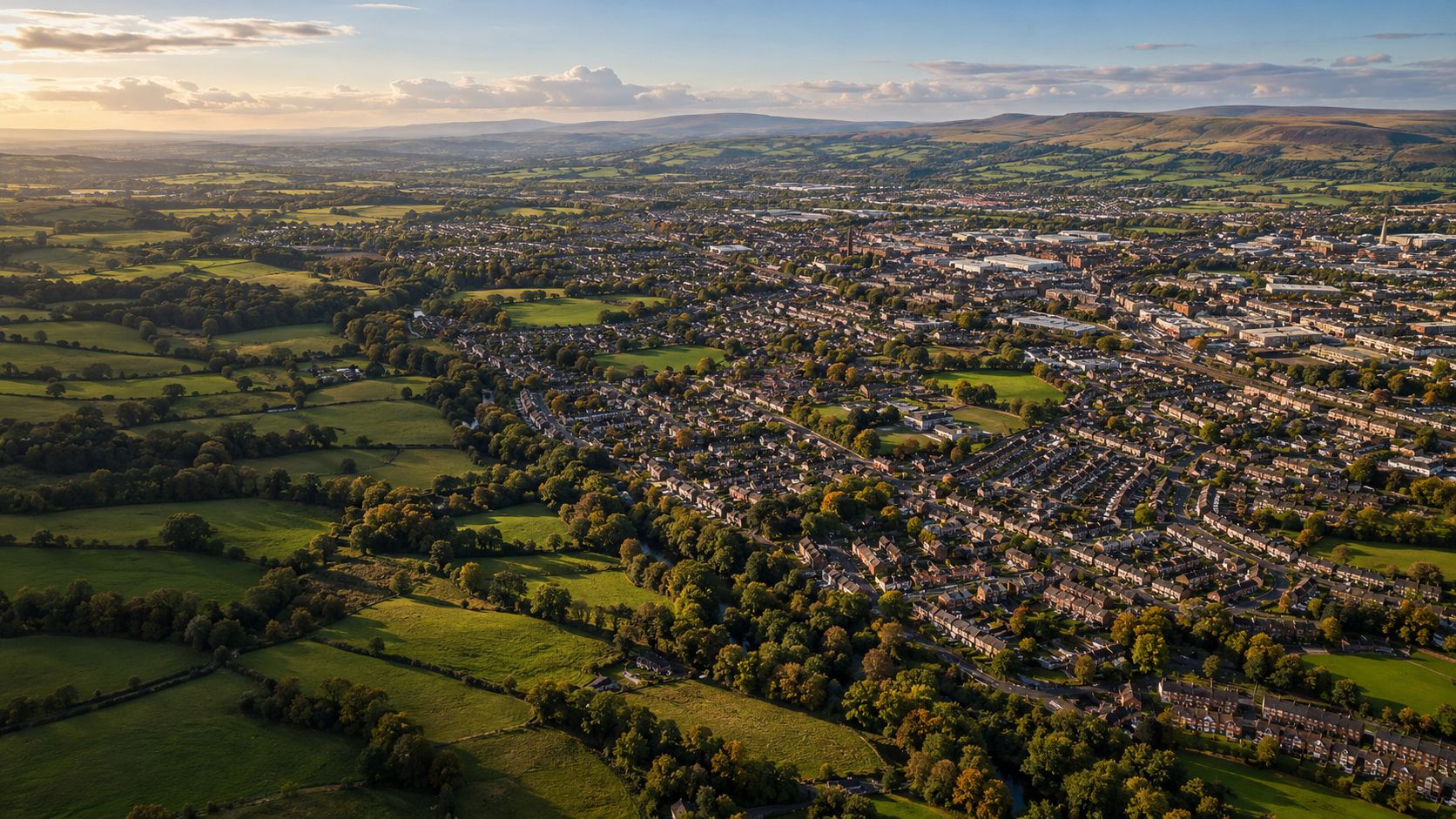 Aerial view of an East Lancashire town surrounded by green fields and moorland at golden hour